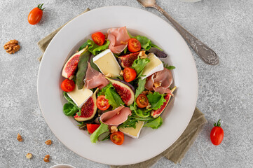 Fresh salad with figs, prosciutto or jamon, brie cheese, tomatoes and walnuts on a concrete background.