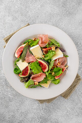Fresh salad with figs, prosciutto or jamon, brie cheese and walnuts on a concrete background.
