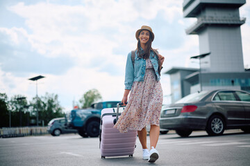 Carefree woman with luggage on parking lot at airport.