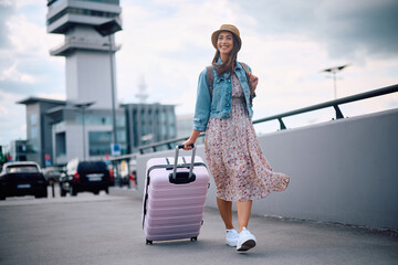 Happy female traveler with suitcase arriving at airport.