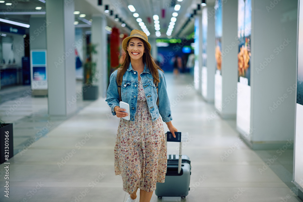 Wall mural Happy traveler pulling her luggage while walking through departure area.