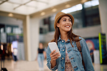 Happy female traveler with cell phone at airport looking away.