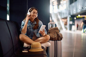 Happy woman using cell phone while listening music over headphones at  airport.