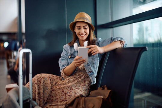 Happy female traveler texting on cell phone at airport.