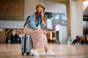 Happy woman communicating on mobile phone while waiting for her flight at airport.