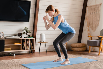 Sporty fit young woman in tracking suit athlete doing sit-ups at home on fitness mat, training her...