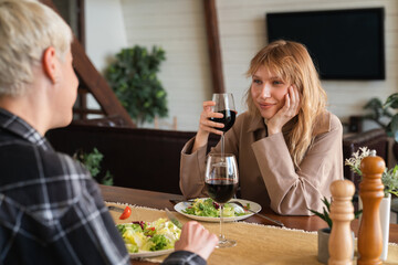 Cheerful young caucasian female LGBT lovers, romantic lesbian couple. Passionate girlfriends talking on date with wine showing support and love