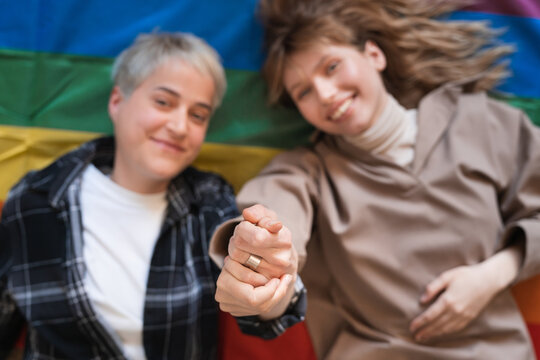 Young transgender lesbians couple two girlfriends holding hands together lying on LGBT rainbow flag protesting for their sexual minorities rights. Gays and lesbians freedom in love