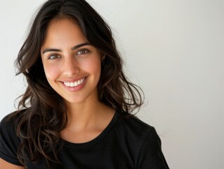 Fototapeta premium Beautiful natural brunette woman, smiling and looking in camera with white teeth. Close-up portrait of cute female woman in black t-shirt on white background. 