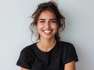 Fototapeta premium Beautiful natural brunette woman, smiling and looking in camera with white teeth. Close-up portrait of cute female woman in black t-shirt on white background. 