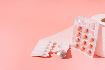 Tablets, rectal candles and ointments in packaging and toilet paper on a pink background.