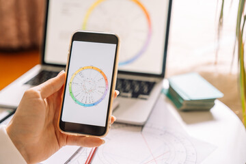 An astrologer draws up a natal chart using a laptop and smartphone.