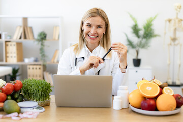 Mature dietitian working with laptop computer making balanced corrective diet plan for patient or...