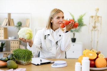 Mature female doctor nutritionist holds fresh organic tomatoes and cabbage in hands while sitting...