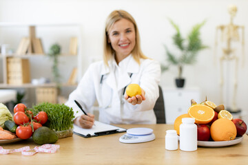 Portrait of smiling female nutritionist doctor sitting at table with vegetables and fruits in...