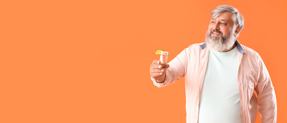 Portrait of senior man with shot of tequila on orange background