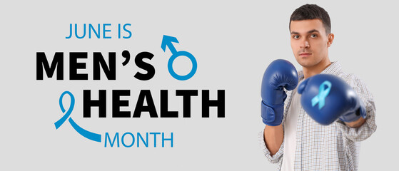 Young man in boxing gloves with blue ribbon on light background. Prostate cancer awareness concept