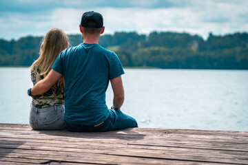 A couple sits on a wooden bridge by the lake in warm summer weather. Thinking one on one with...