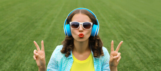 Portrait of happy smiling young woman listening to music in headphones on grass in summer park