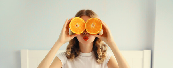 Happy healthy cheerful young woman covering her eyes with slices of orange fruits and looking for