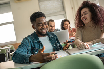 Couple of students working together on some task. They're sitting in a classroom and learning together.	
