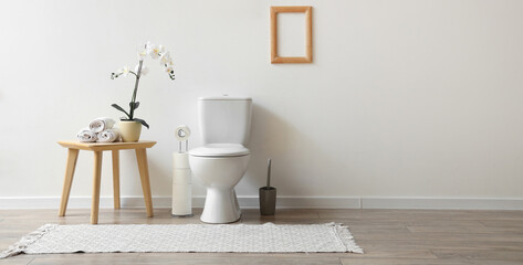 Interior of restroom with toilet bowl and table with orchid and towels near white wall. Banner for...