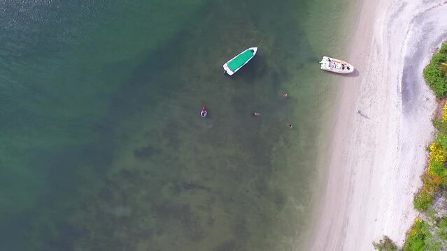 Pessoas em lanchas tomando banho de mar em praia paradis&iacute;aca de uma pequena ilha na Bahia, Brasil. Imagem a&eacute;rea azimutal de um drone voando alto.