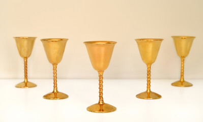 Five golden antique goblets with high stems on the white table. Close-up. Selective focus. Copy space. 