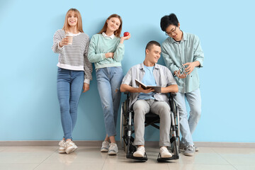 Group of teenagers with boy in wheelchair near blue wall