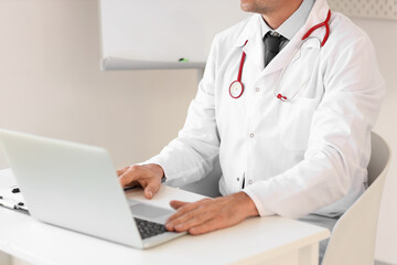Mature doctor working with laptop at desk in medical office, closeup