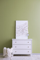 Modern chest of drawers with canvas and basket near green wall