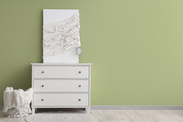 Modern chest of drawers with canvas and basket near green wall