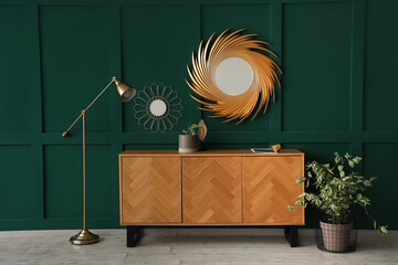 Wooden cabinet with lamp and mirrors near green wall