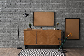 Wooden cabinet with frames and lamp near grey brick wall