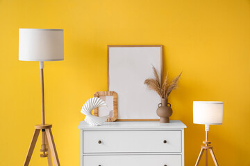 Cabinet with lamps and frames near yellow wall