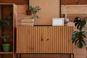 Cabinet with flowerpots and frames near wooden wall