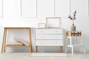 Cabinet with frames, ladder and table near white wall