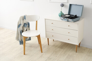 Cabinet with record player and chair near white wall