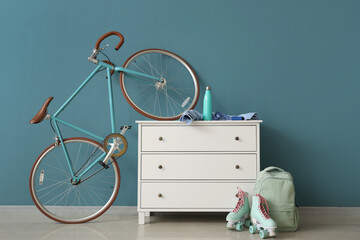 Cabinet with bike, roller skates and backpack near blue wall