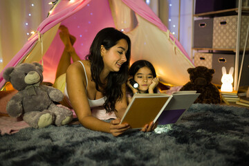 Latin woman and her daughter bonding over a book in a cozy, softly lit bedroom at night, cherishing...