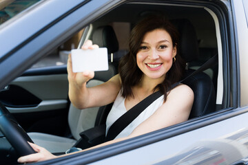 Confident female driver happily displaying her driver's license in her car, radiating positivity on the road