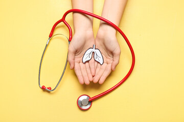 Female hands with paper lungs and stethoscope on yellow background