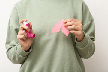 Young woman with paper lungs and asthma inhaler on white background