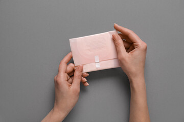 Female hands with menstrual pad on grey background
