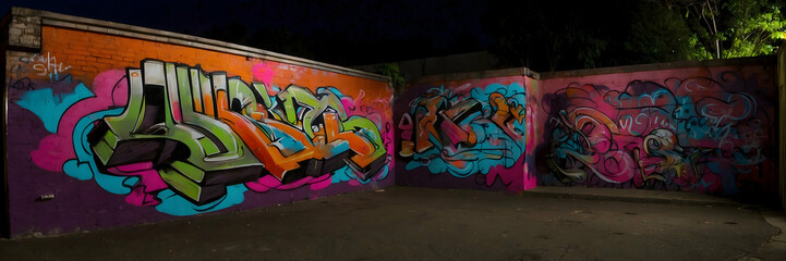 Nighttime panoramic shot capturing vibrant graffiti art on a wall within an urban environment