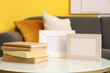 Blank photo frames with books on table in living room, closeup