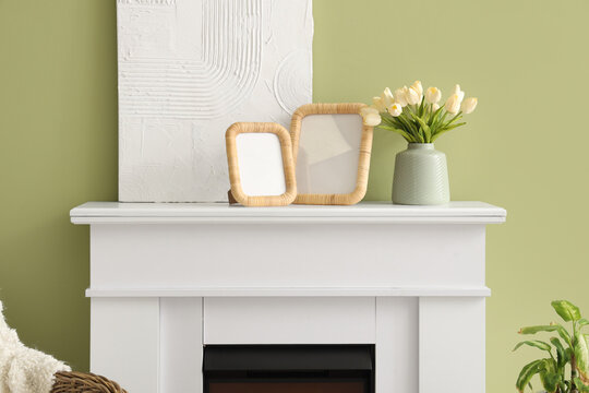 Blank photo frames, painting and vase with tulips on mantelpiece in living room