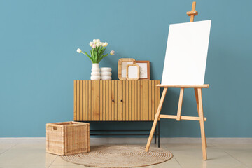 Interior of living room with easel, tulips and frames on commode