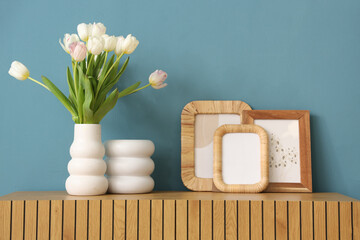 Photo frames and vase with tulips on commode near blue wall