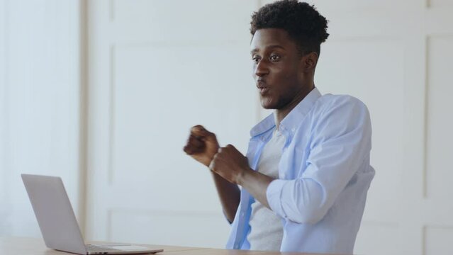 Happy emotional african american guy dancing, reading great news on laptop